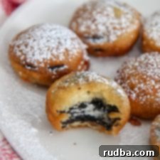 deep fried Oreos with powdered sugar on a white plate with one half eaten cookie and a red and white towel on the side.