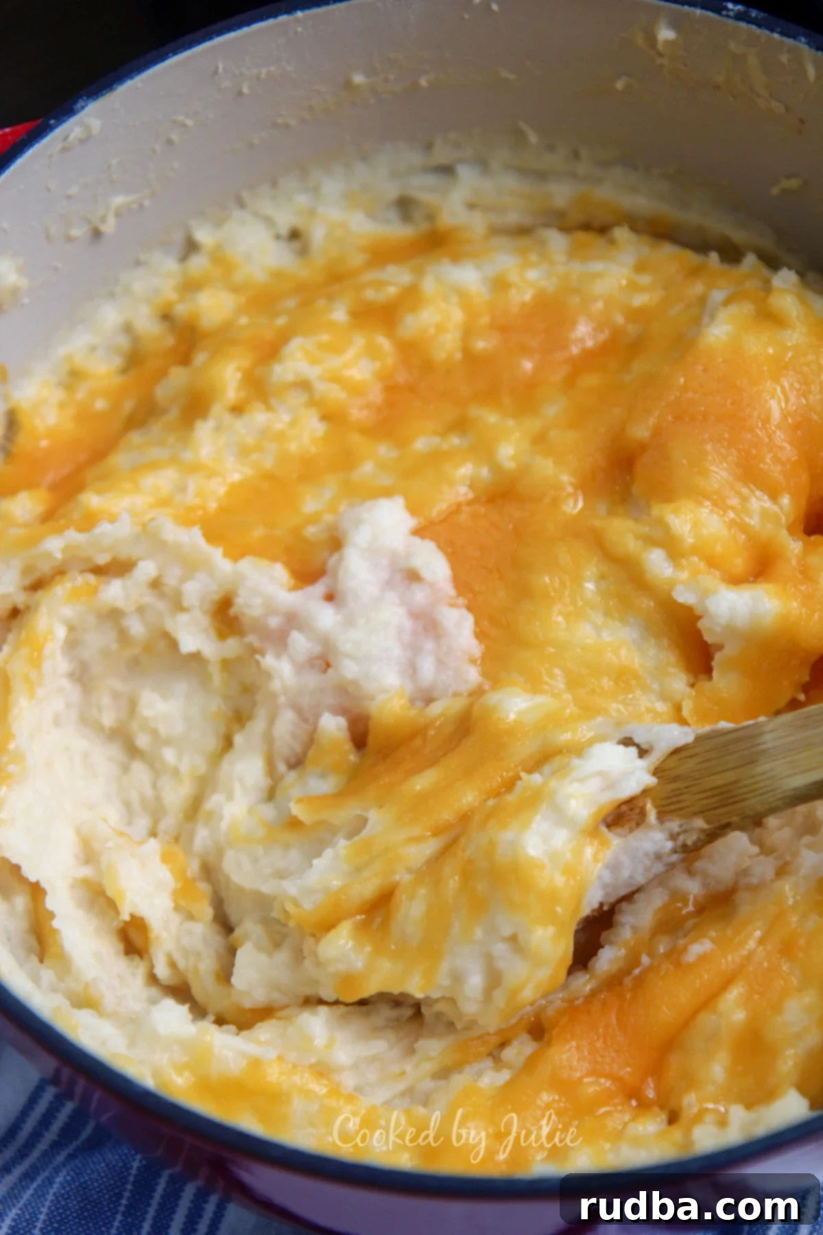 cheddar garlic mashed potatoes in a red dutch oven and wooden spoon