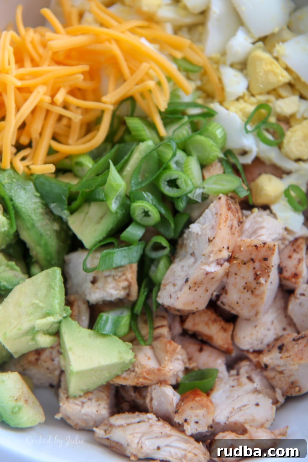 baked chicken, avocados, scallions, cheddar cheese, and boiled eggs in a white bowl