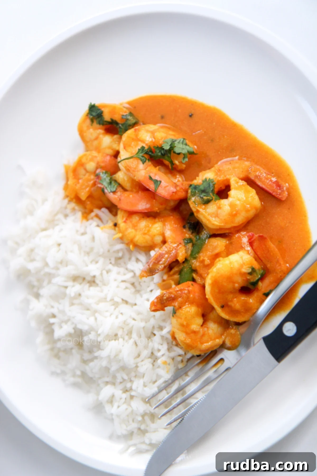 coconut shrimp curry with white basmati rice on a white plate with utensils