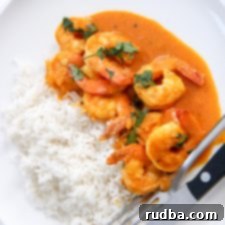 coconut shrimp curry with white basmati rice on a white plate with utensils