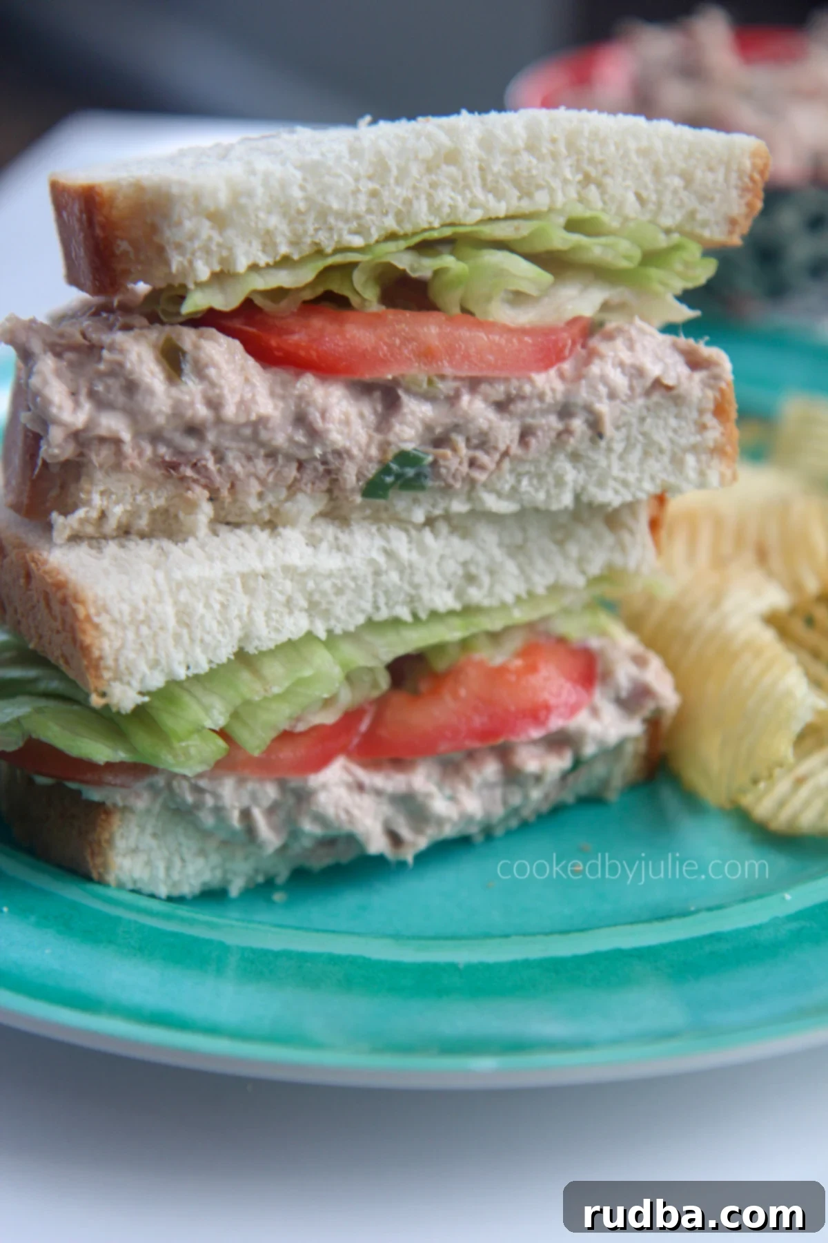 tuna salad sanwiches stacked on a blue plate with potato chips on the side 