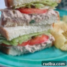 tuna salad sanwiches stacked on a blue plate with potato chips on the side