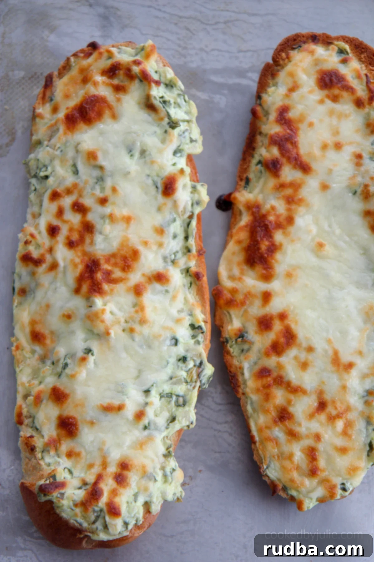 Two loaves of cheesy spinach artichoke bread on a baking sheet, golden and bubbly.