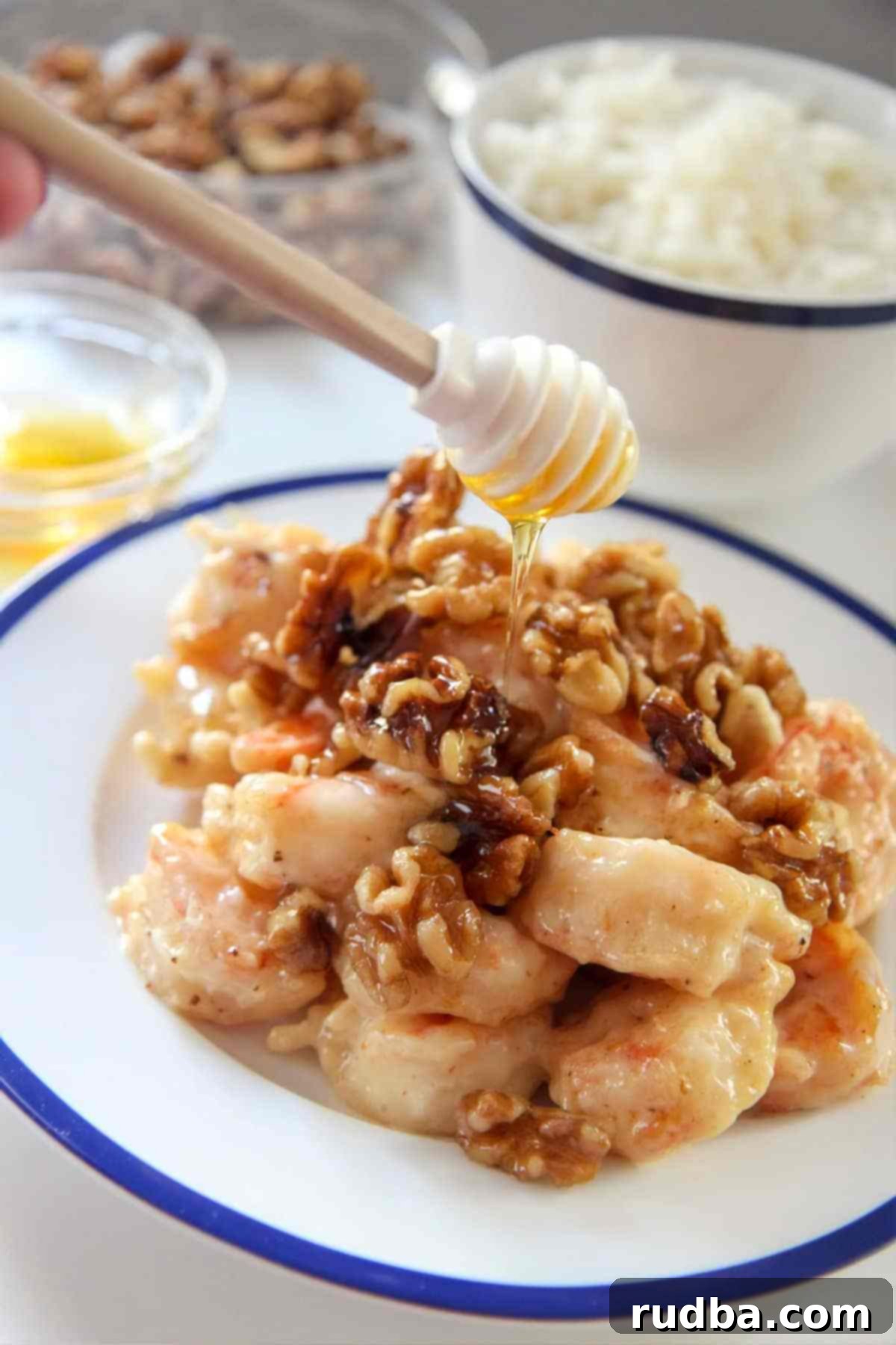 Honey Walnut Shrimp on a white and blue plate with a honey dipper, showcasing the crispy texture and glossy sauce.