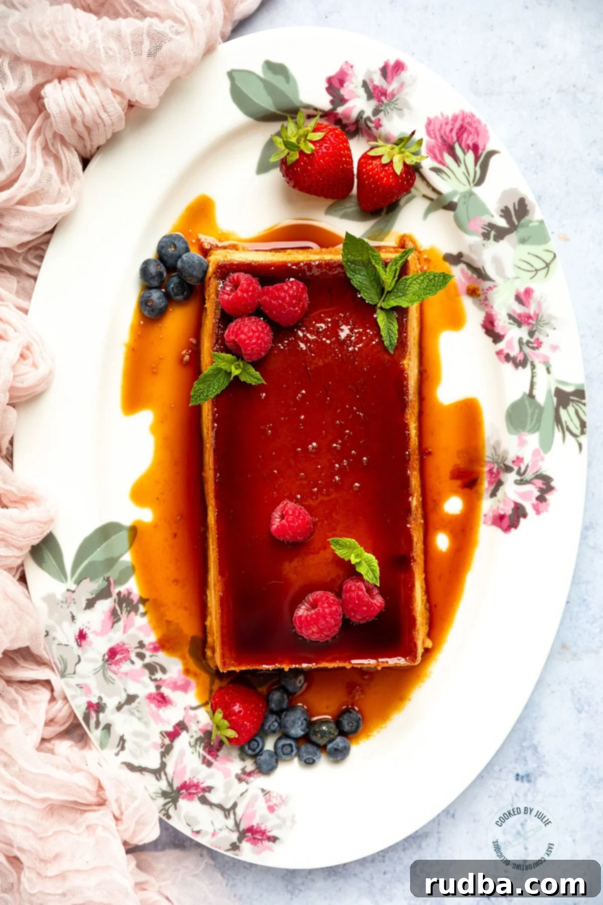 Crème Caramel 2 Flan with caramel, fresh berries, and a sprig of mint on a pristine white platter with a pink towel on the side. The rich golden caramel beautifully contrasts with the vibrant red berries, promising a delightful dessert experience.
