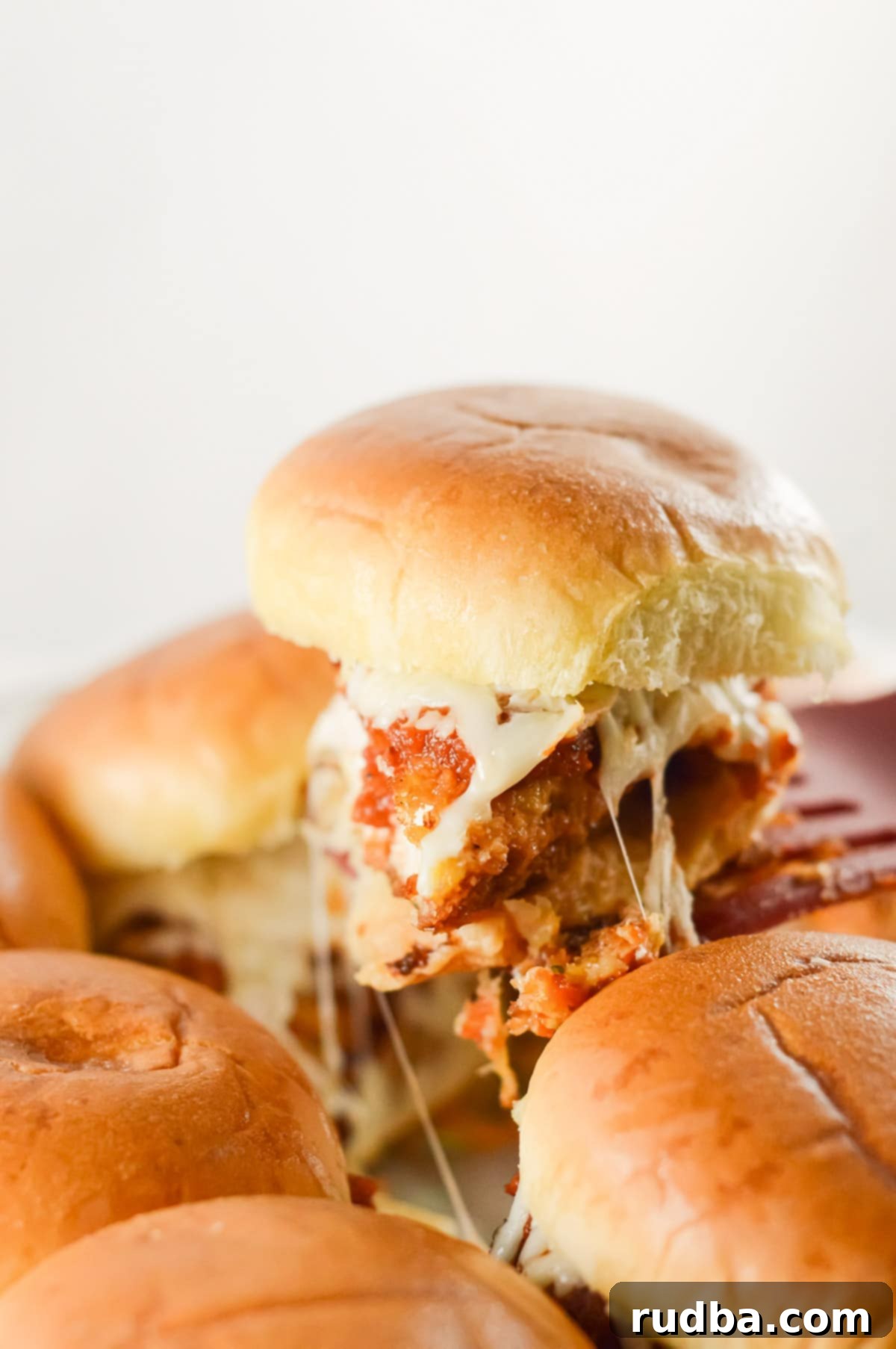 A spatula gently lifting a golden-brown chicken parm slider from a baking pan, revealing melted cheese and perfectly cooked chicken.