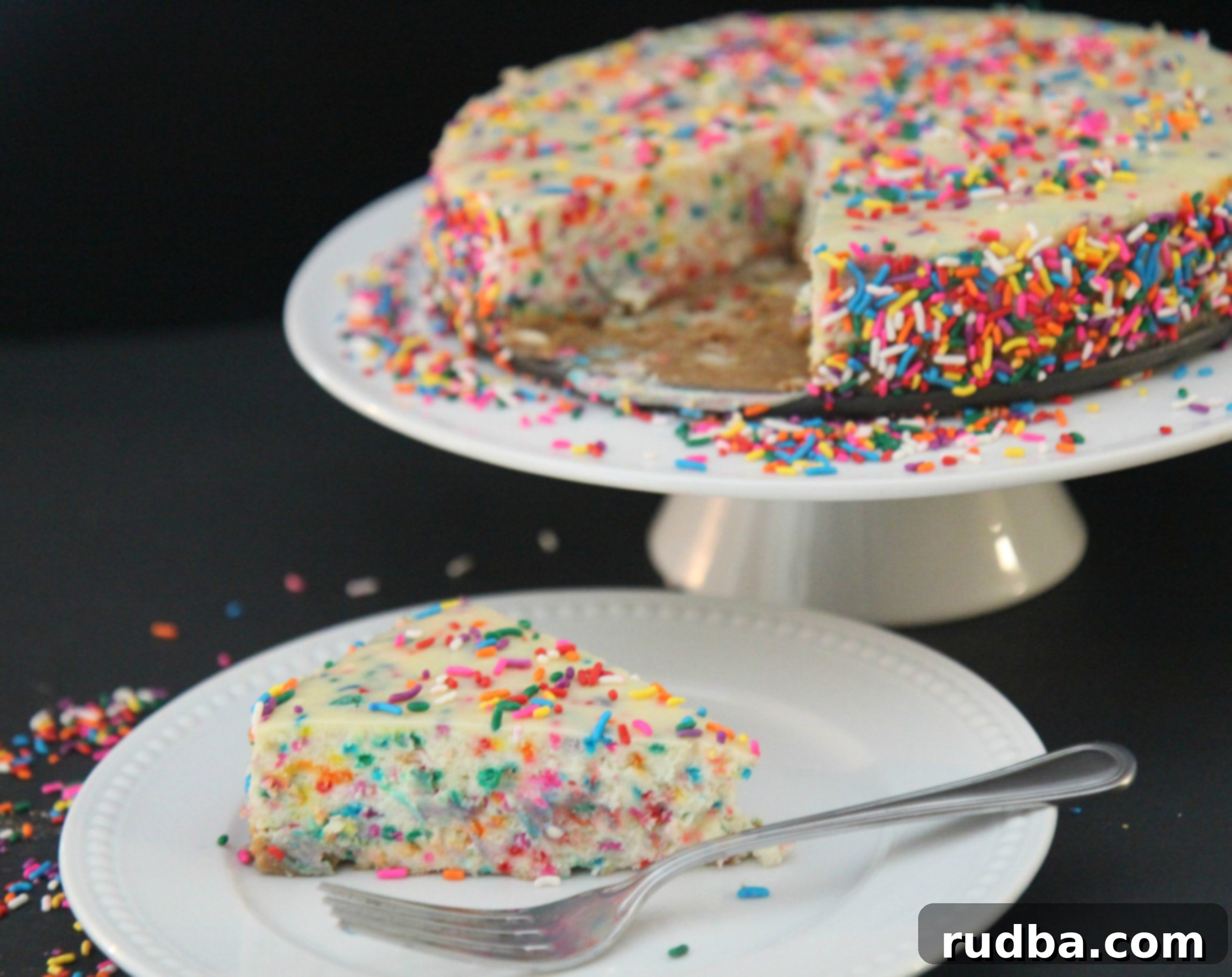 An entire Funfetti Cheesecake, decorated with a generous amount of rainbow sprinkles on top, inviting guests to celebrate.