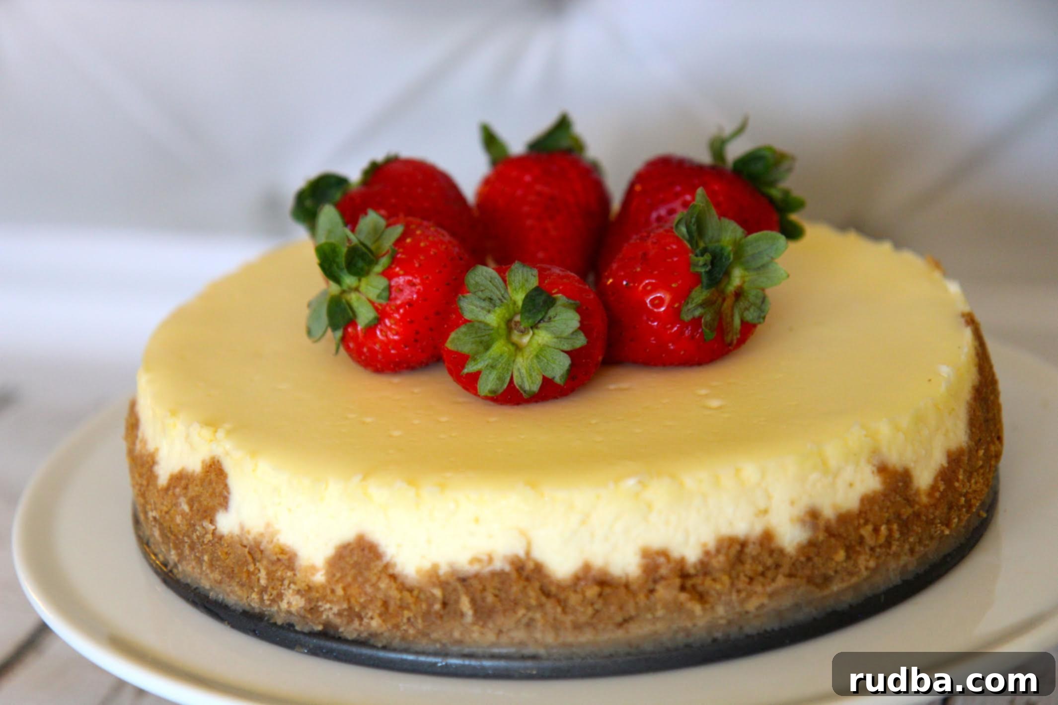 Plain Homemade cheesecake with a graham cracker crust and topped with strawberries.