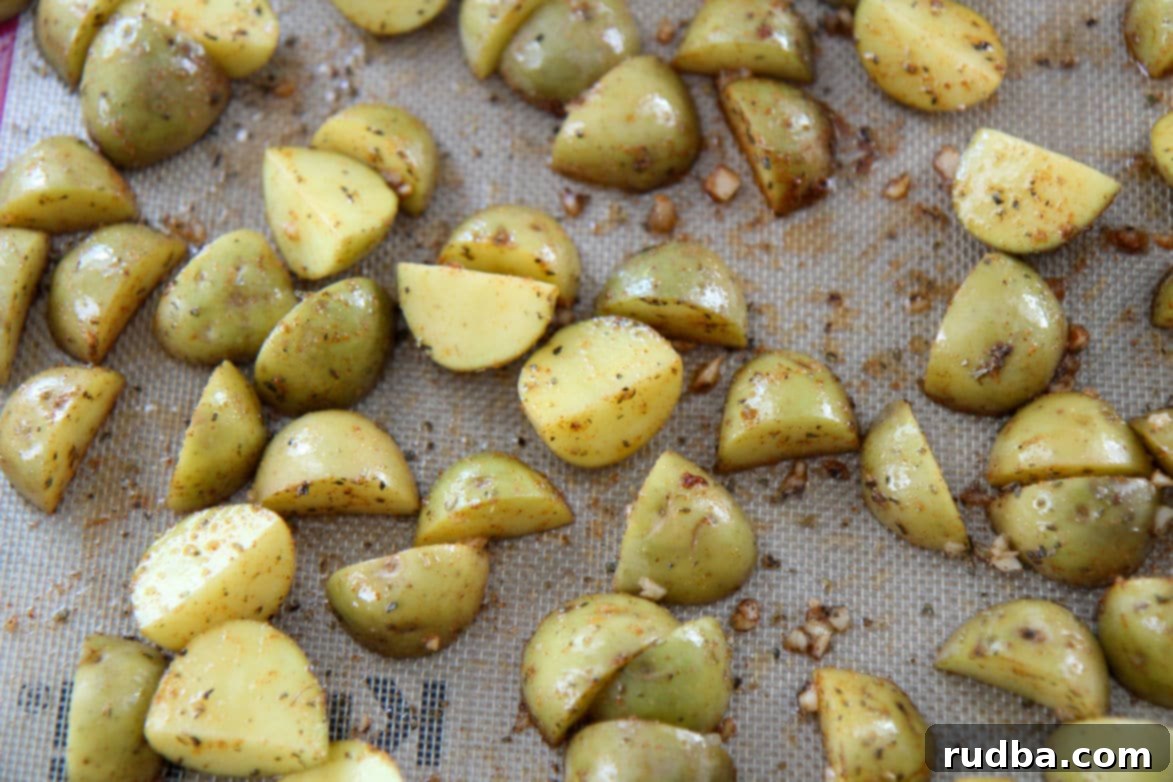 Close-up shot of perfectly seasoned yellow baby potatoes glistening on a baking sheet, showcasing their vibrant color from the spices and oil, having just come out of the oven.