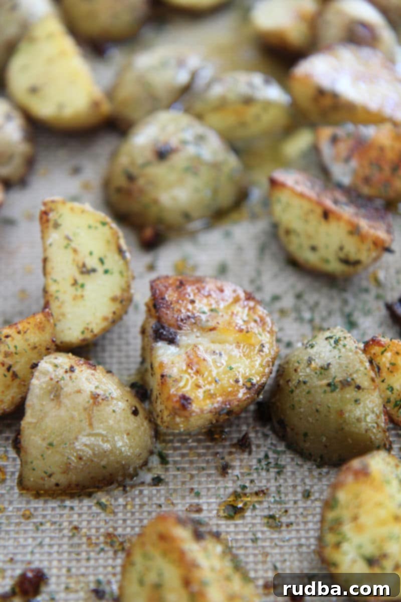 A vibrant close-up of a serving of roasted garlic potatoes on a baking sheet, with individual pieces showing their crispy edges and seasoning, ready to be enjoyed.