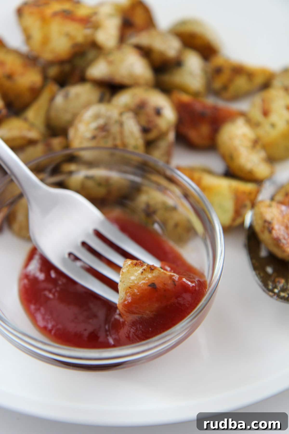 A fork holding a single perfectly roasted potato, freshly dipped in a dollop of bright red ketchup, illustrating a common and delicious way to enjoy the dish.