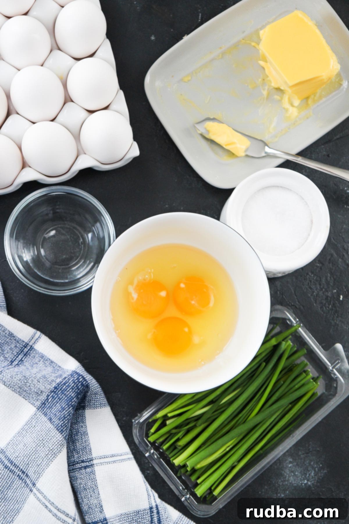eggs in a bowl, chives, salt, water, and a blue and white cloth