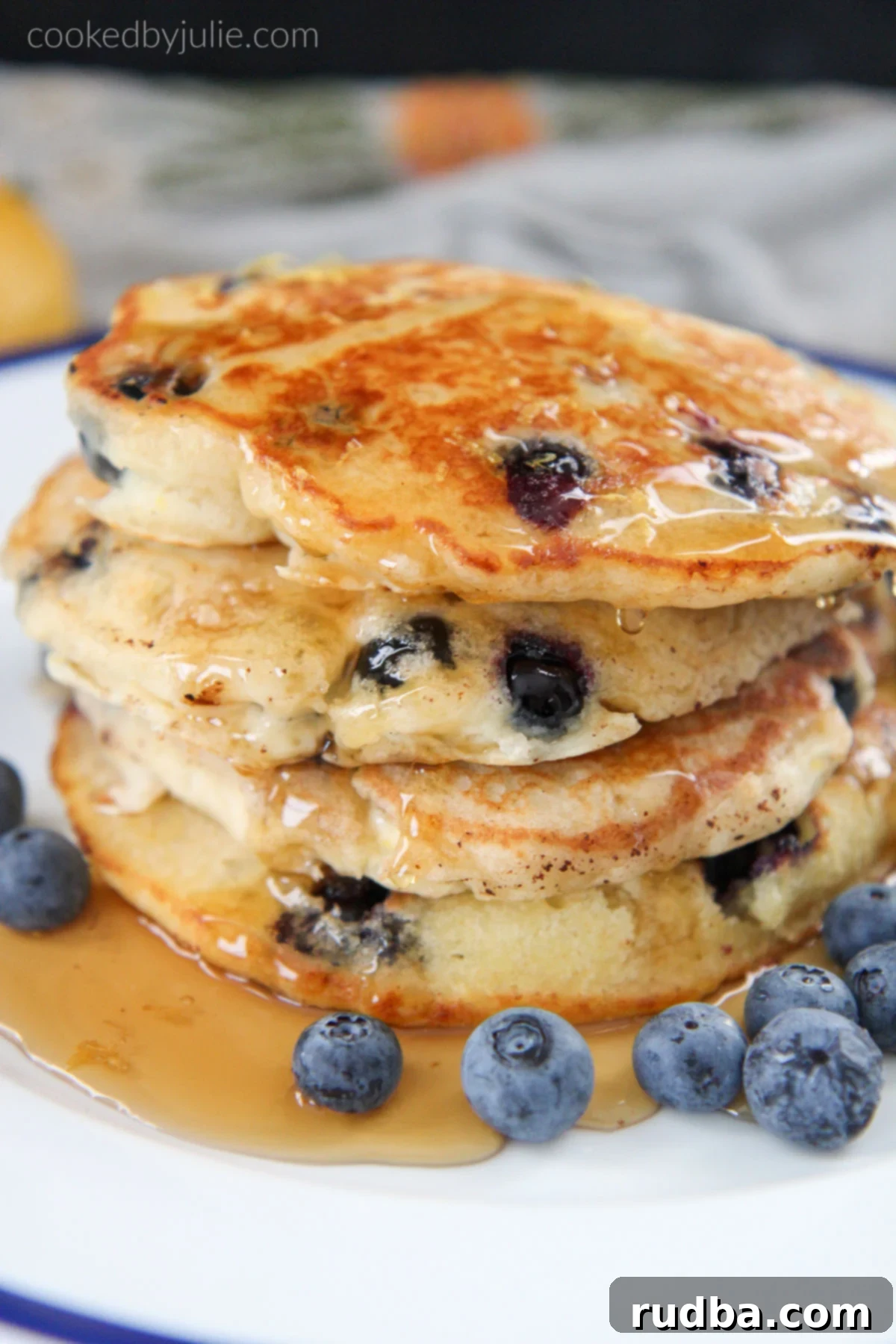 Stacked fluffy lemon blueberry pancakes drizzled with maple syrup and fresh blueberries on the side, ready to be served.