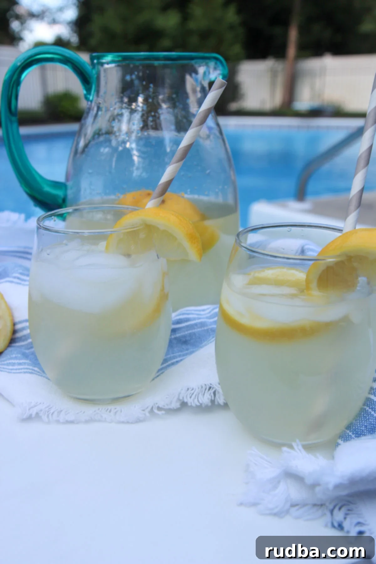 two glasses of lemonade and a glass pitcher in the background