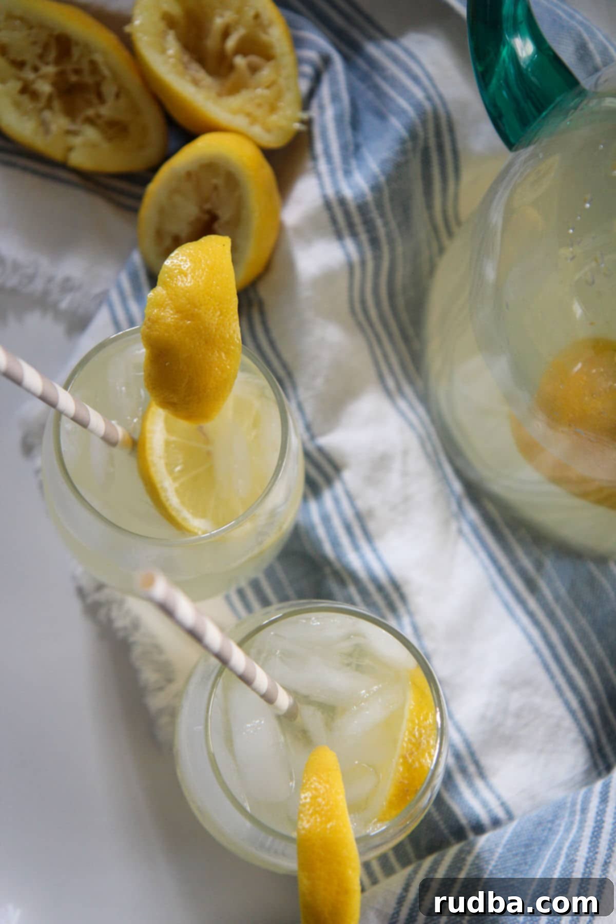 2 glasses of lemonade with straws on a white table with a blue table cloth