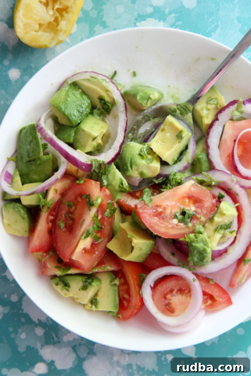 tomatoes and avocado salad in a white bowl with a lemon on the side 