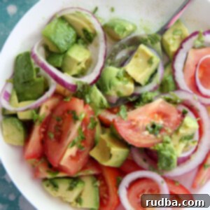 tomatoes and avocado salad in a white bowl with a lemon on the side