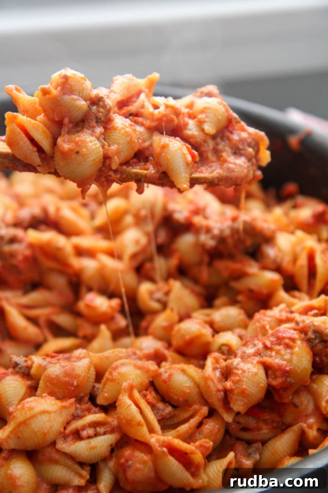 A spoonful of creamy beef and shells being lifted from a skillet