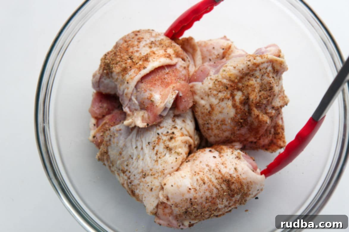 seasoned chicken thighs in a glass bowl with red tongs 
