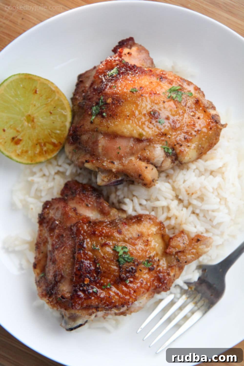 two honey lime chicken thighs on top of rice on a white plate with a fork and lime wedge 