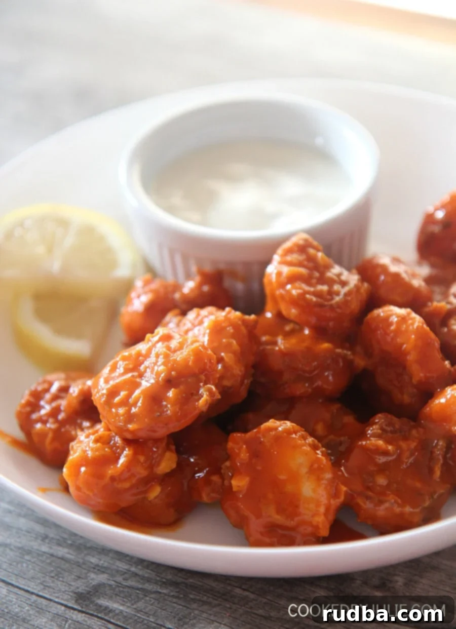 crispy buffalo shrimp with lemon slices and a side of bleu cheese dip in a white bowl.