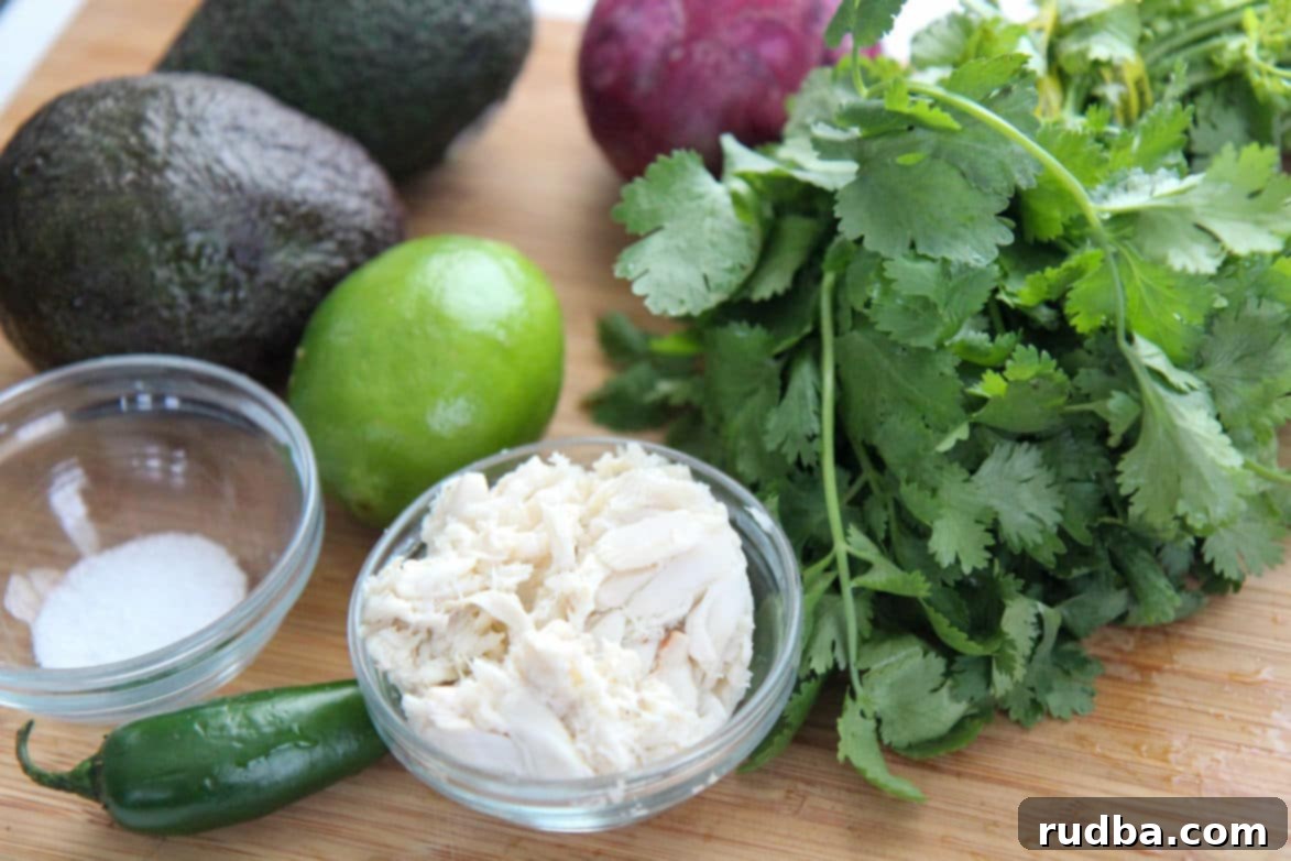 Fresh ingredients laid out for crab guacamole preparation: lump crab meat and sea salt in small bowls, alongside vibrant cilantro, juicy lime halves, creamy avocados, and a whole green jalapeno pepper.