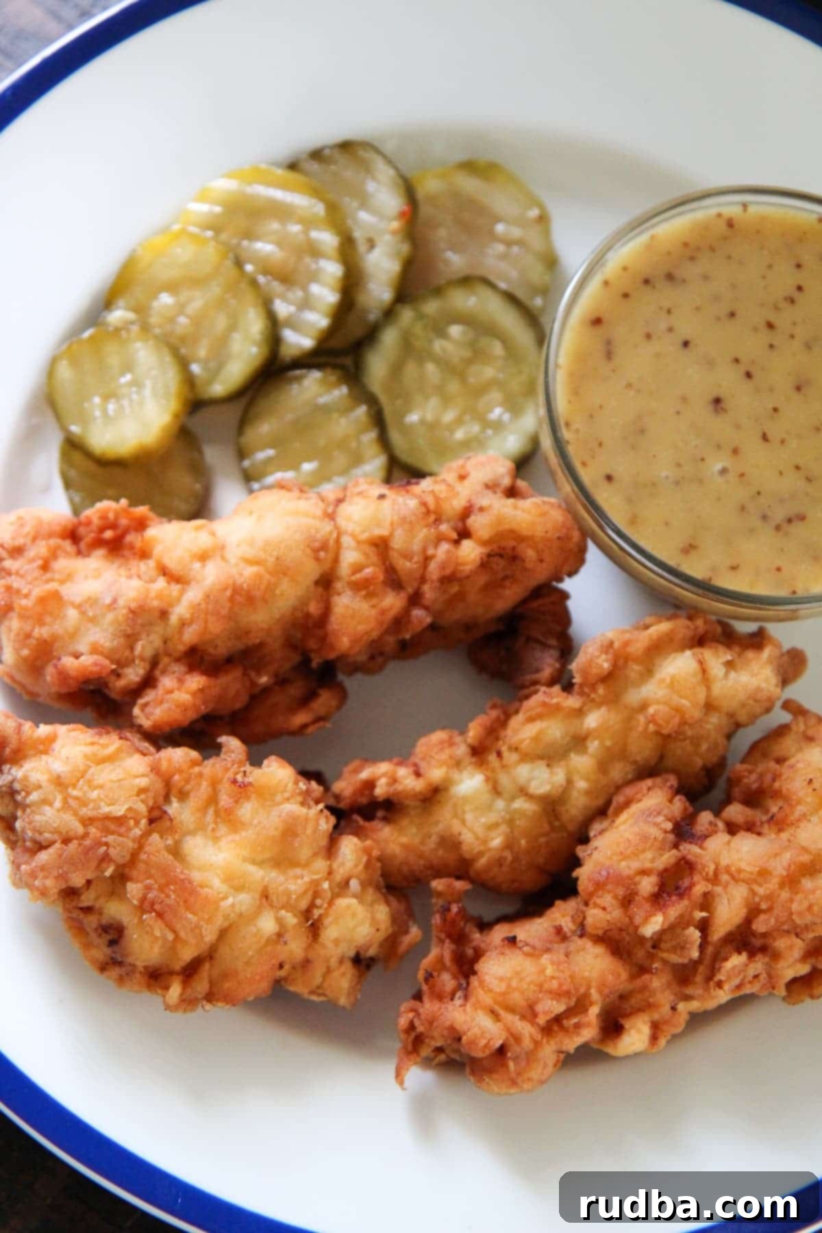 chicken strips, honey mustard, and pickles on a white plate