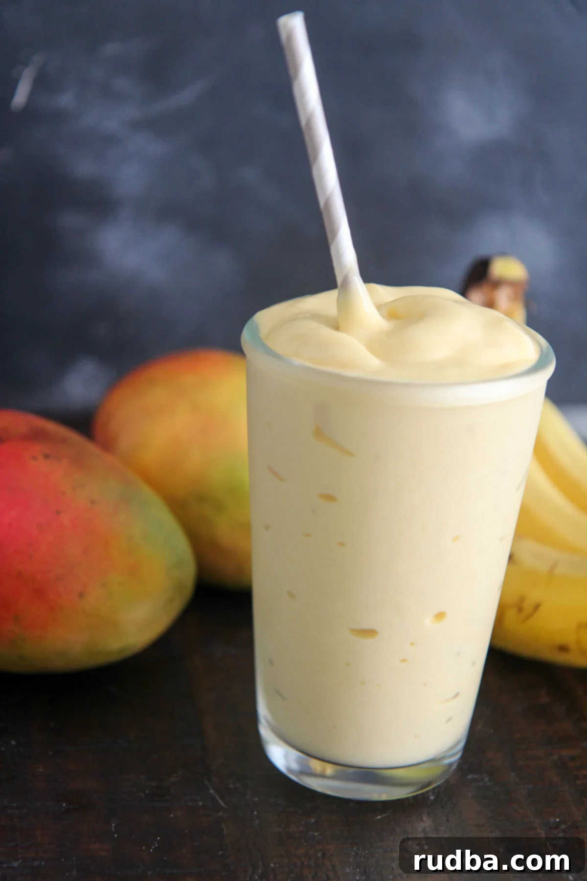 mango smoothie in a glass with a straw and fruits in the background
