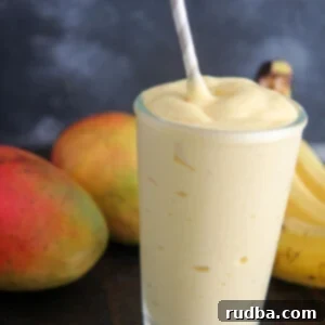mango smoothie in a glass with a straw and fruits in the background