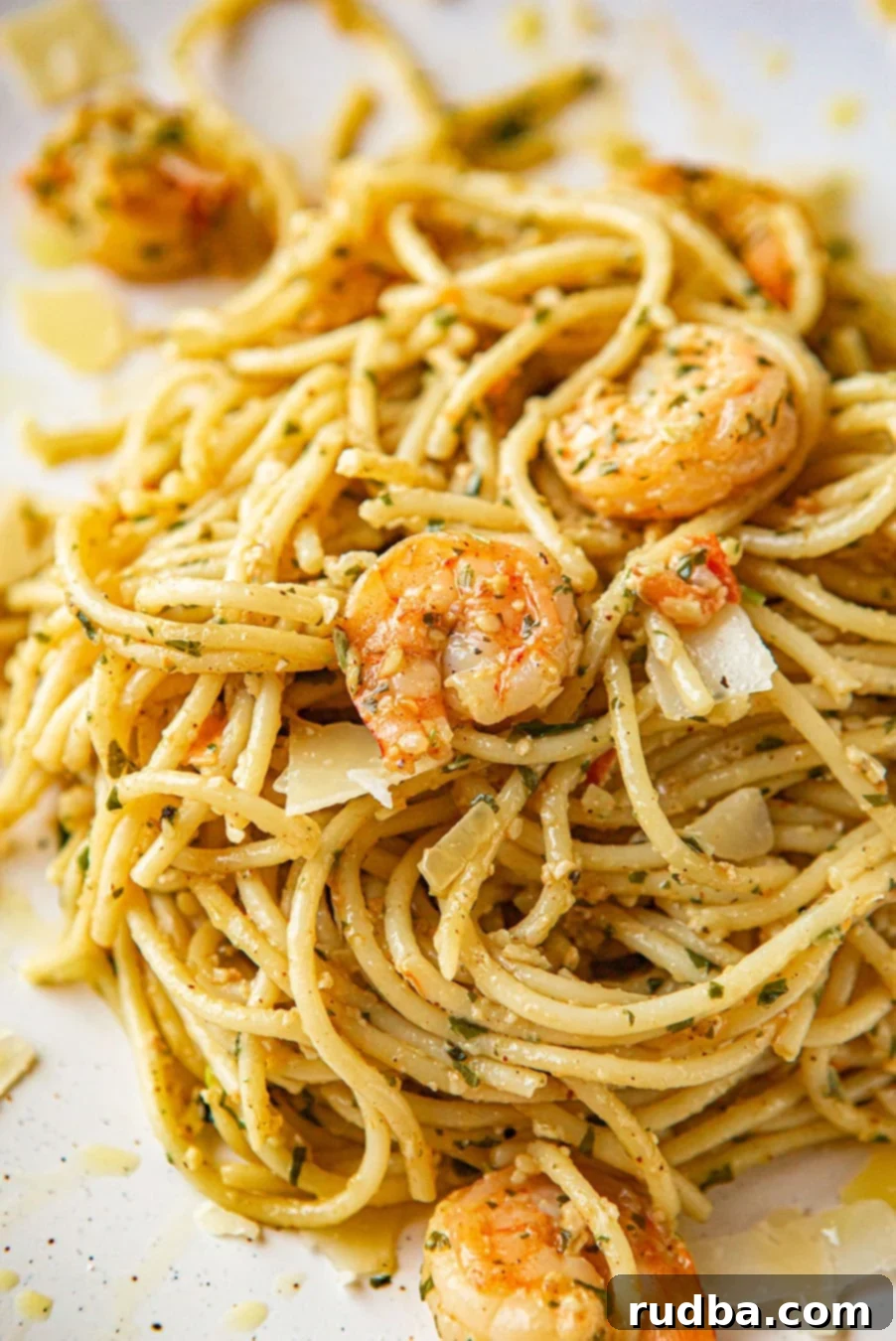 Close-up shot of a white plate filled with shrimp pesto spaghetti, garnished with fresh basil leaves.