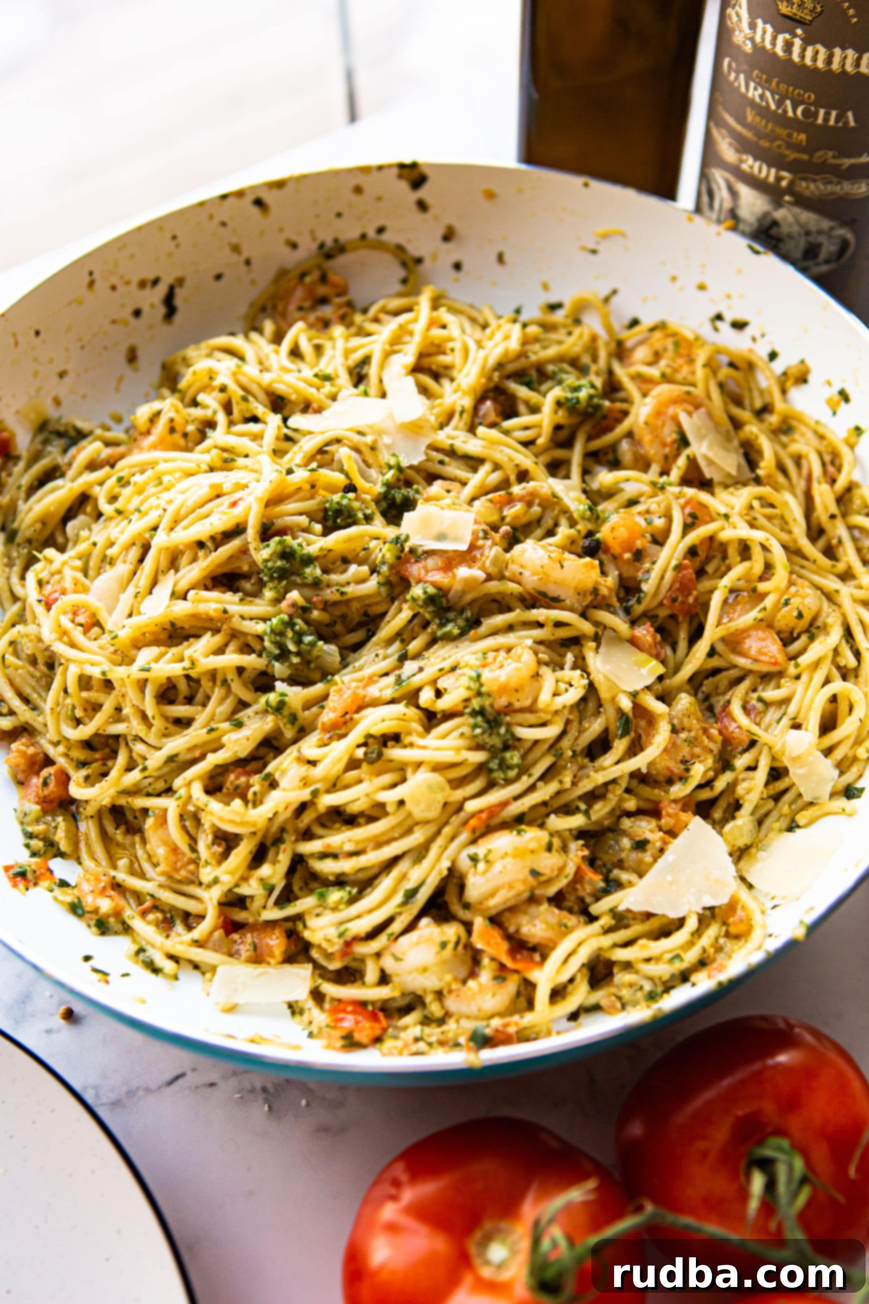 Pesto shrimp pasta cooking in a large non-stick skillet, with tomatoes and cream visibly mixed in.