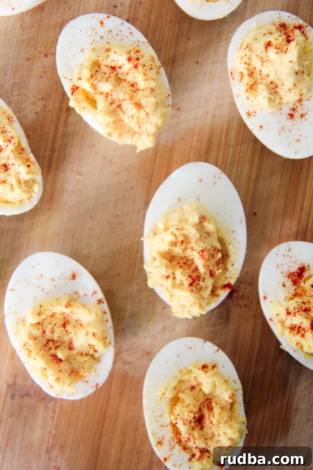 A platter of beautifully arranged deviled eggs, some sprinkled with paprika, on a dark wooden cutting board, ready for a gathering.