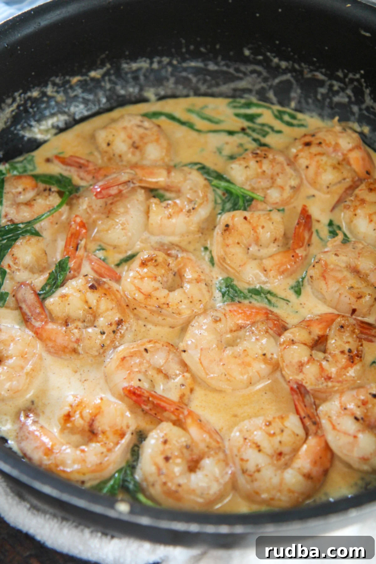 Tender shrimp, creamy sauce, and fresh spinach in a black skillet, ready to be served
