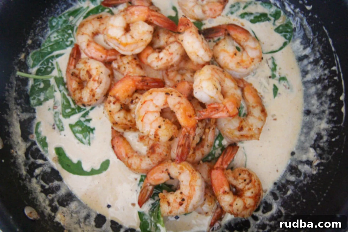Close-up shot of creamy garlic shrimp with spinach in a black skillet, highlighting the rich texture