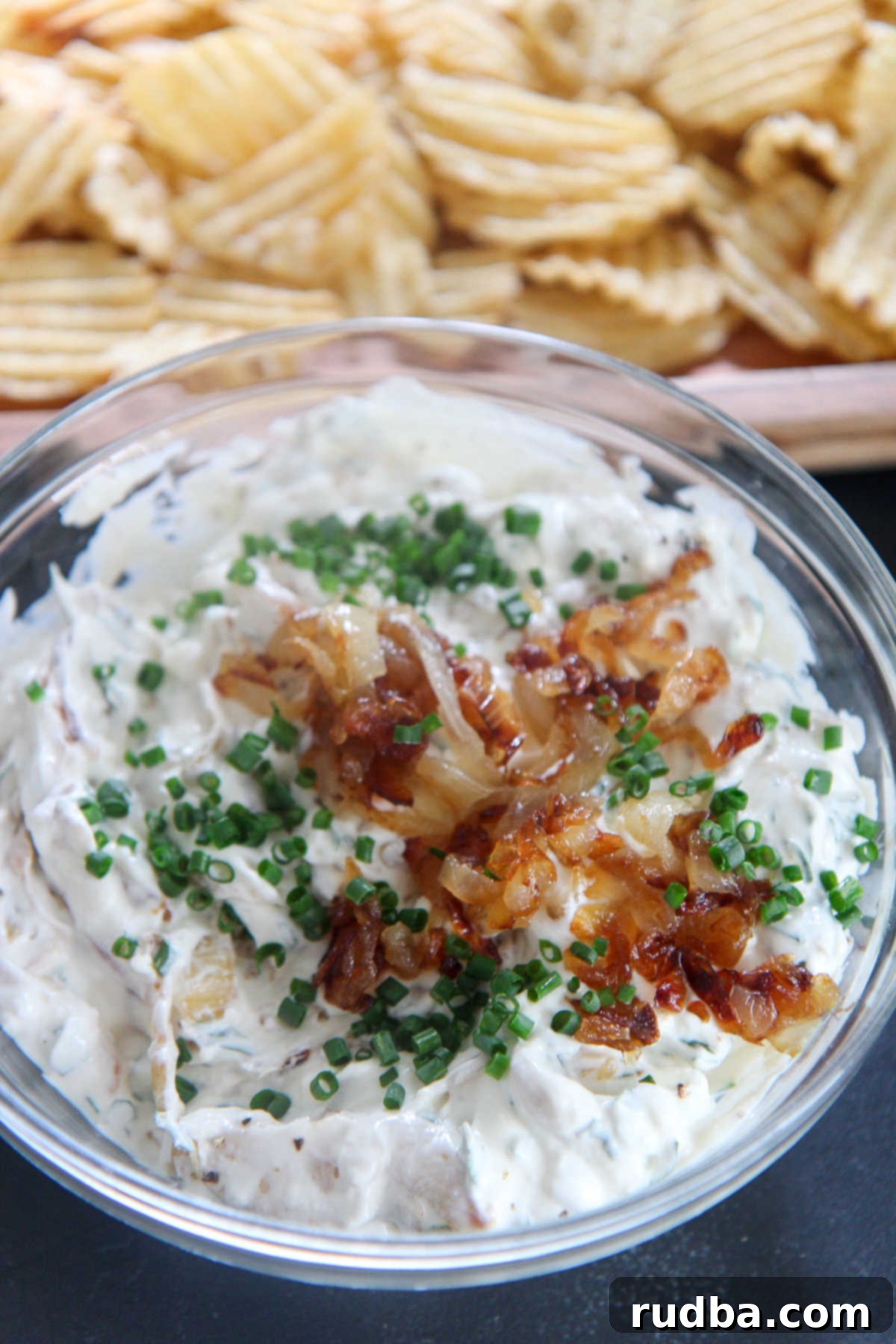 Potato chips and French onion dip in a clear bowl with chives and onions