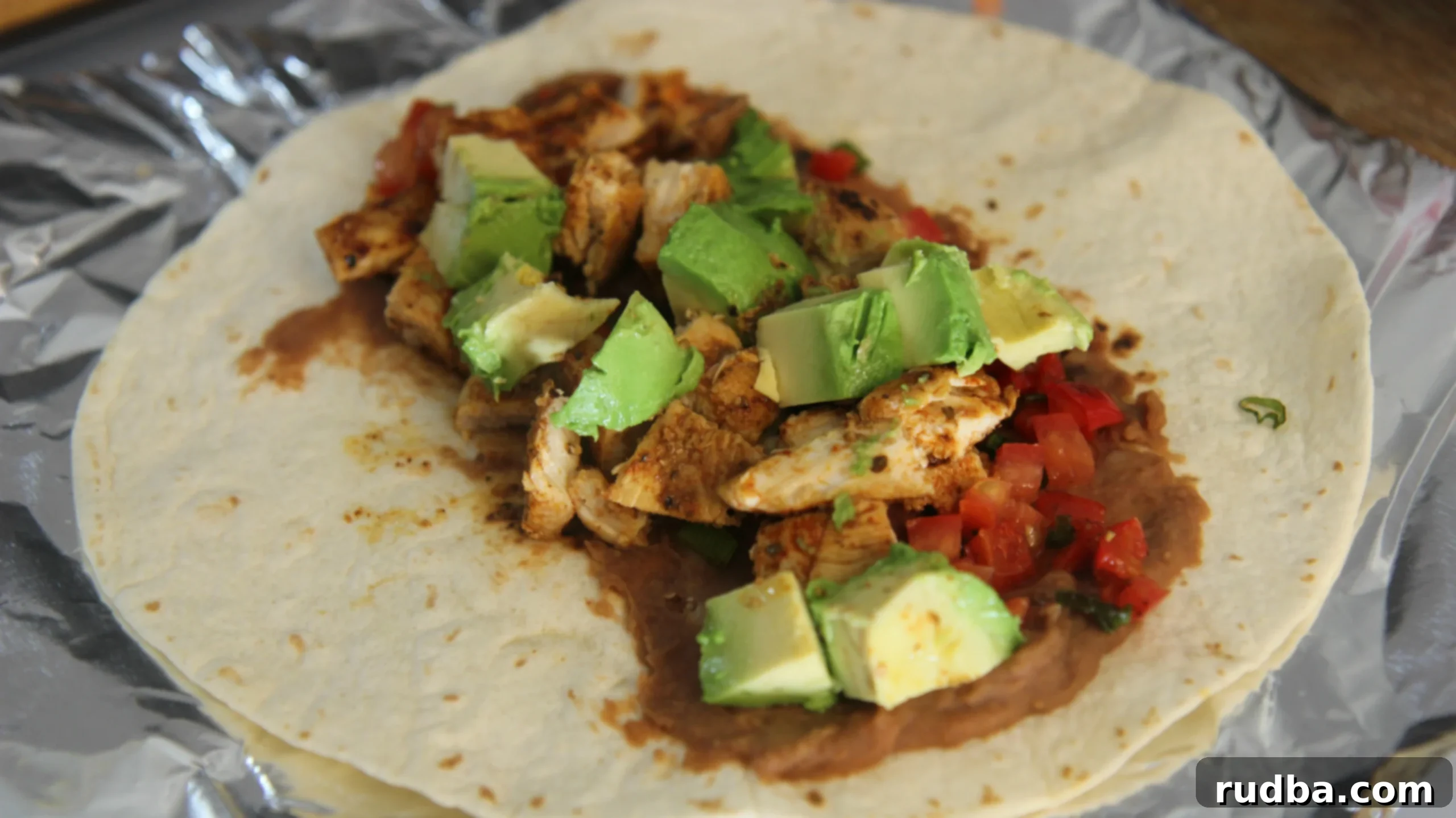 Add the chicken to a tortilla with refried beans, avocado chunks and some tomatoes. 