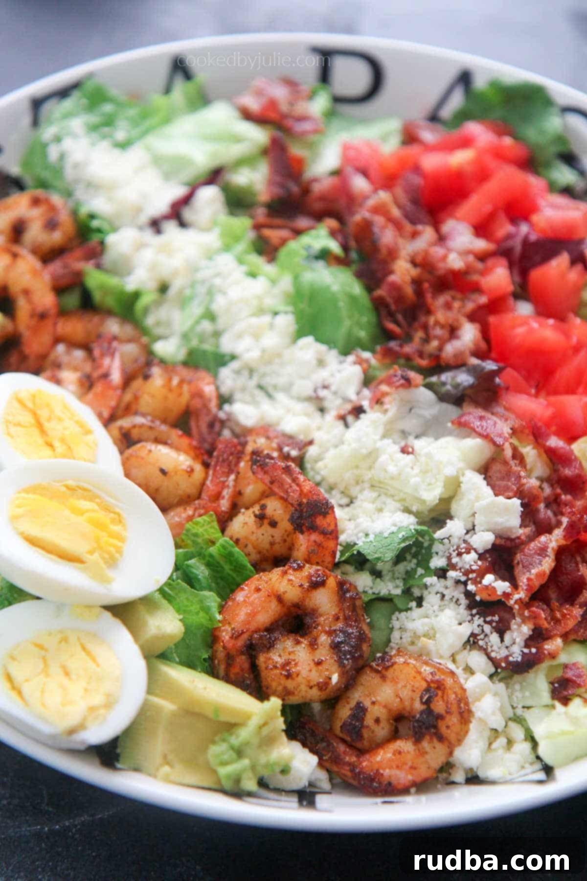 Beautifully arranged shrimp cobb salad with boiled eggs in a pristine white plate, showcasing vibrant ingredients.
