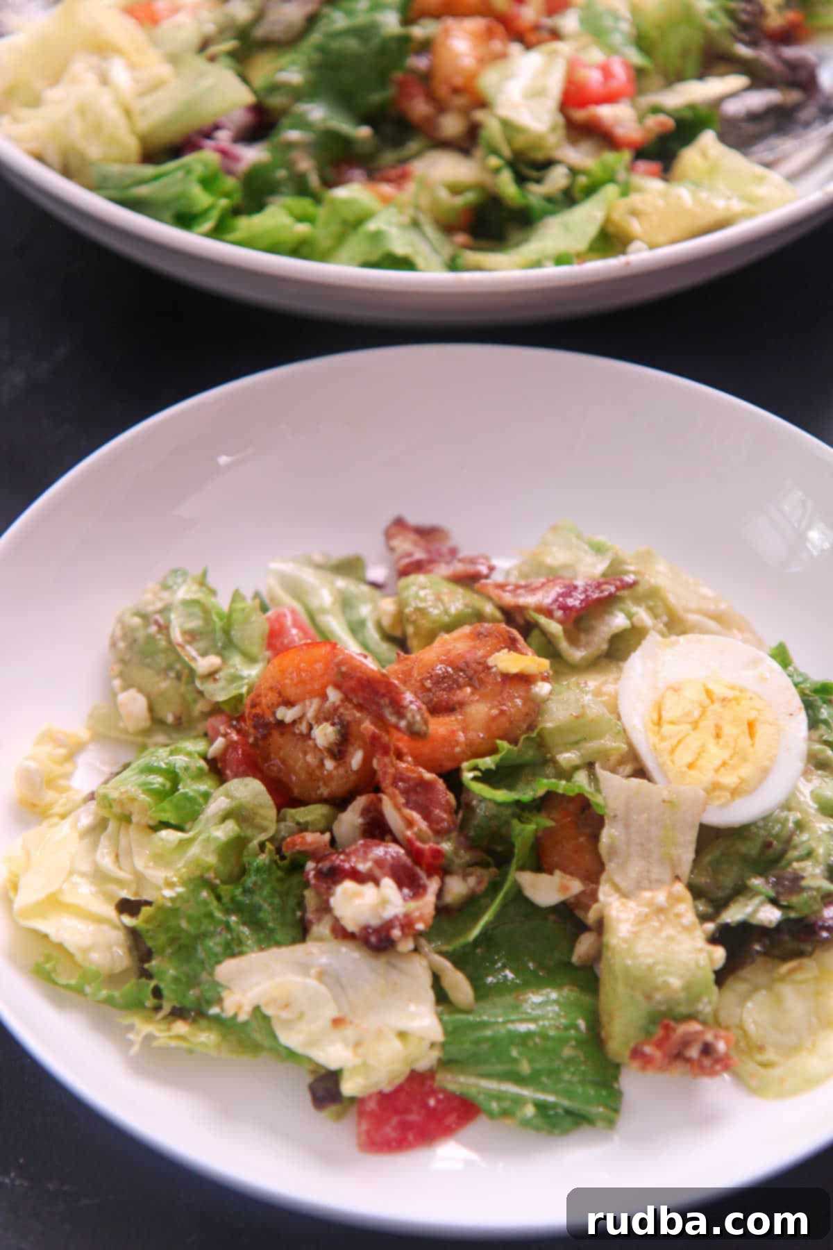 A small portion of shrimp cobb salad elegantly presented on a plate with a fork, with a blurred background of a salad bowl.