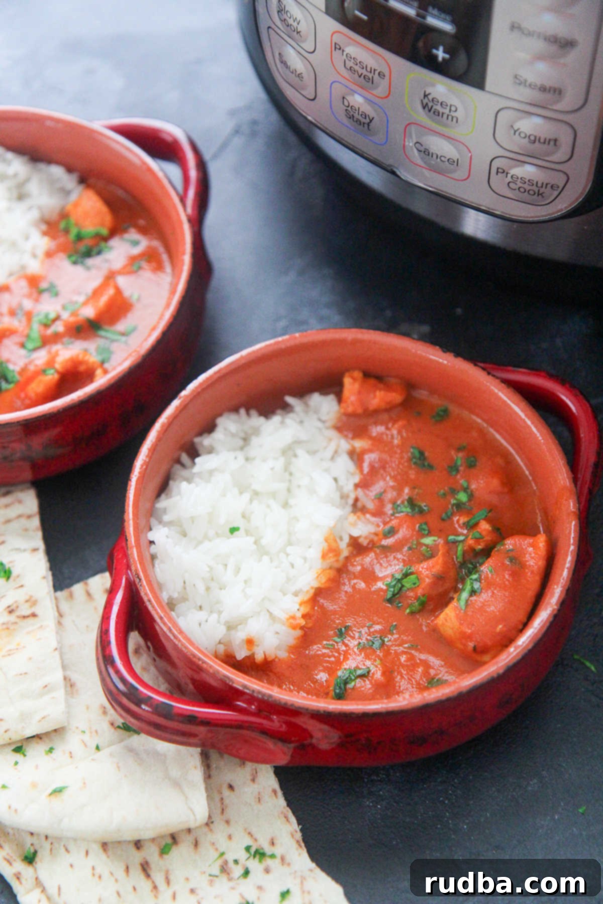Two small bowls of Instant Pot Butter Chicken, garnished with cilantro, served with pita bread and a side of rice, ready to eat.