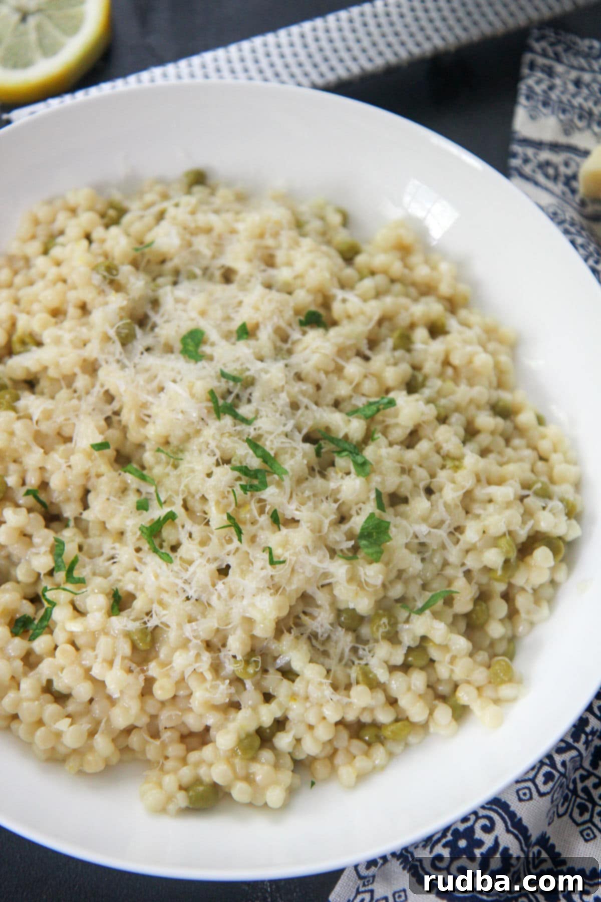 Fluffy Lemon Israeli Couscous with Parmesan cheese and fresh parsley in a white bowl, ready to serve.