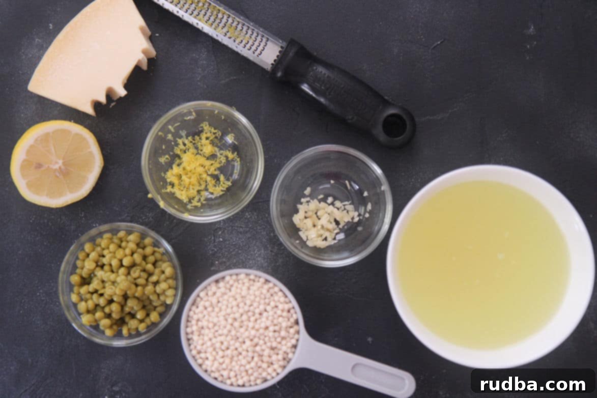 Individual bowls containing chicken stock, Israeli couscous, green peas, a halved lemon, minced garlic, and grated Parmesan cheese.