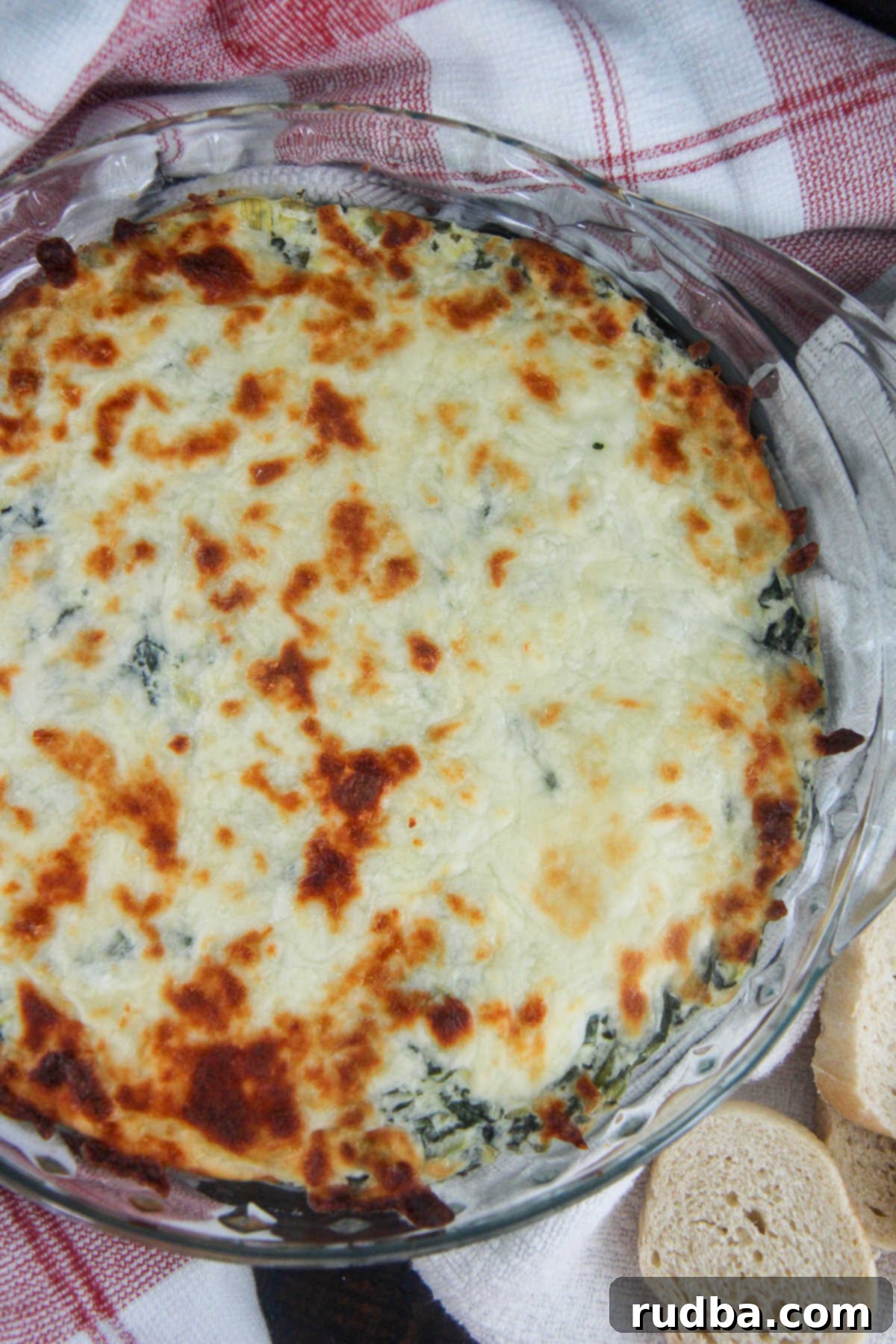 Creamy spinach artichoke dip in a glass bowl, ready to serve with crispy bread slices on the side.