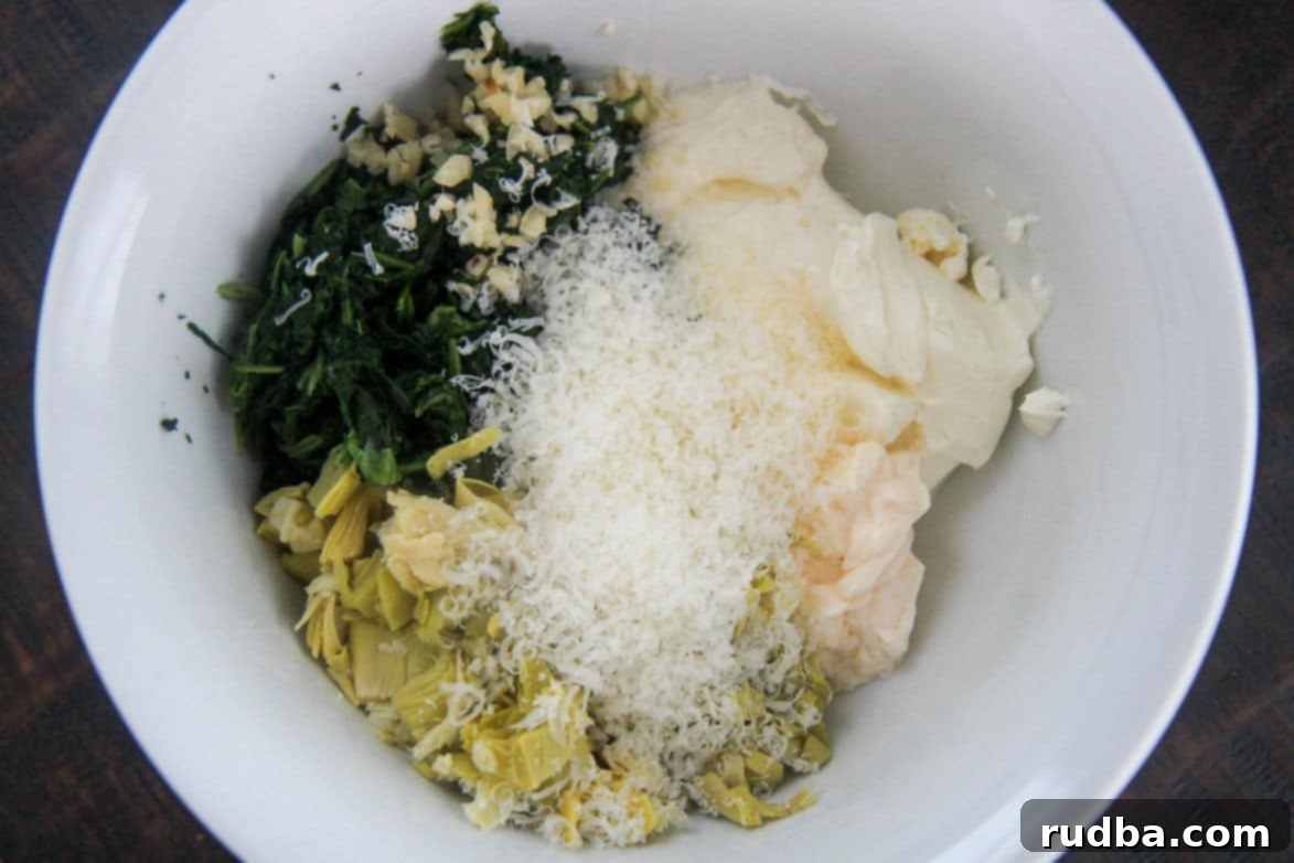 Raw ingredients for spinach artichoke dip: spinach, cheese, and chopped artichokes in a white bowl.