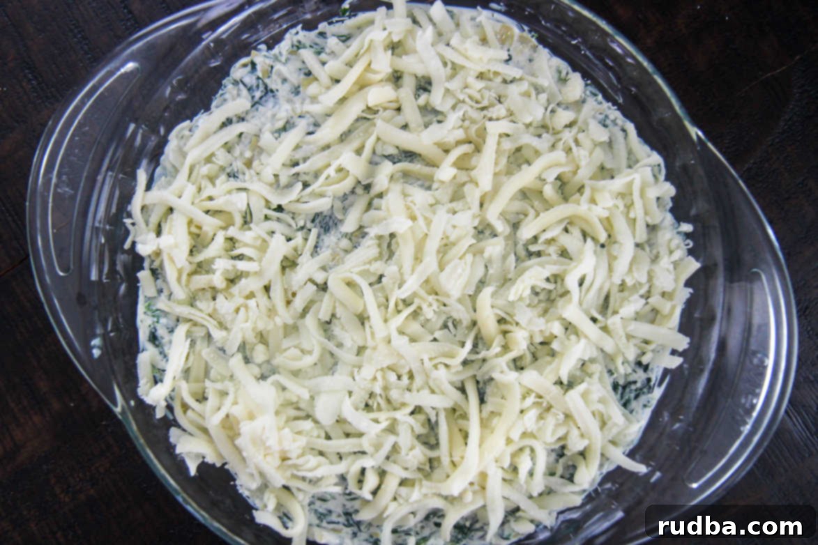 Freshly baked spinach dip with melted mozzarella cheese, bubbling hot in a glass baking dish.