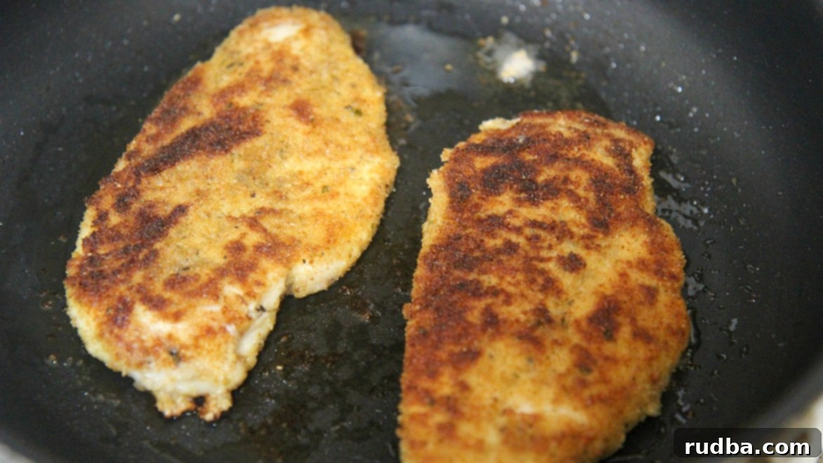 two fried chicken breasts in a black skillet. 