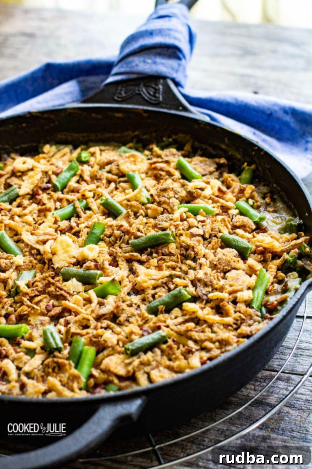 Classic green bean casserole in a rustic iron skillet, garnished with crispy fried onions and a blue kitchen towel