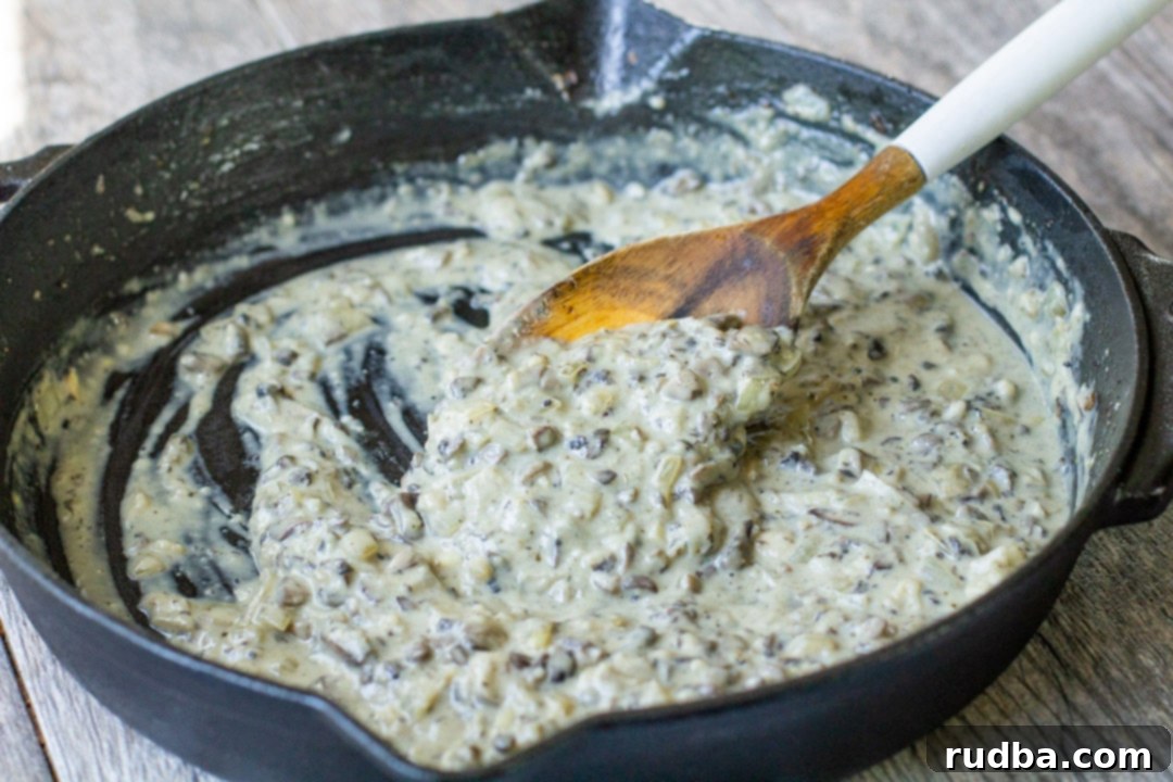 Rich and creamy homemade mushroom sauce simmering in a black iron skillet with a wooden spoon