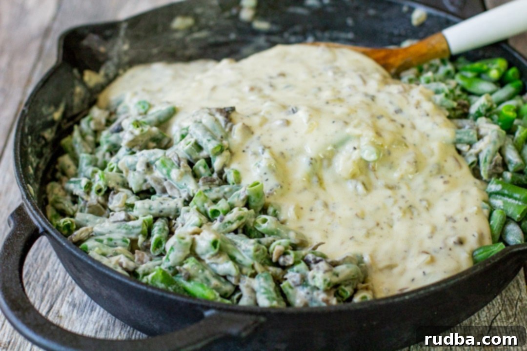 Thawed frozen green beans being gently folded into a luscious homemade cream of mushroom sauce in a black skillet