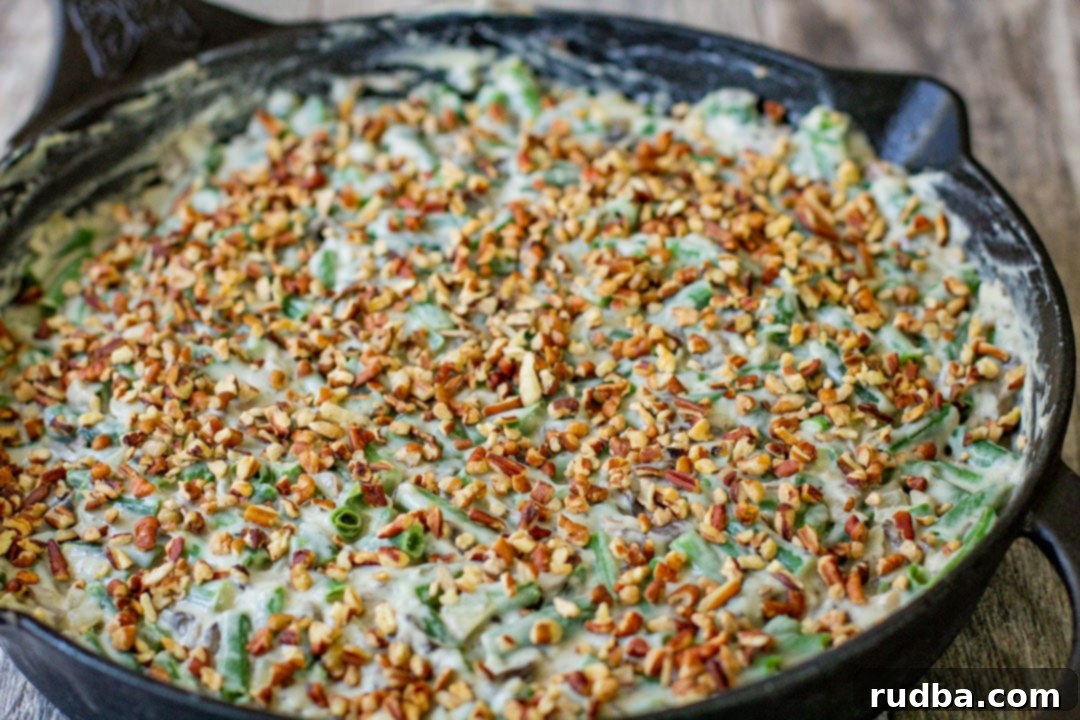 Assembled green bean casserole in a black baking dish, topped with finely chopped pecans before the fried onions